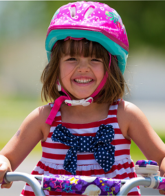 Young girl in pink helmet riding a bike in the park
